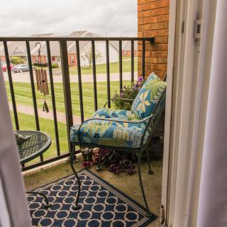 A cozy balcony with a cushioned chair and small table overlooking a grassy area.