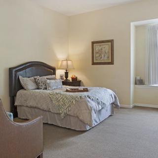 A cozy bedroom with a neatly made bed, nightstand, and comfortable chair.