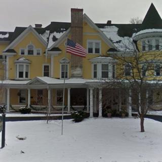 A large yellow house with an American flag in front, surrounded by snow.