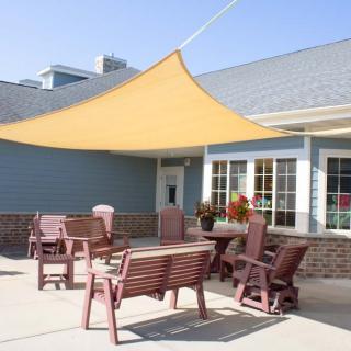 An outdoor patio area with a yellow shade sail, chairs, and a table in front of a building.