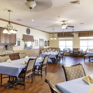 A spacious dining area with neatly arranged tables and chairs, featuring warm lighting and wooden flooring.
