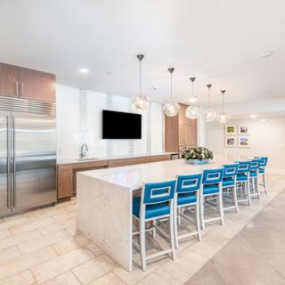 A modern kitchen with a large island, blue bar stools, and sleek pendant lighting.