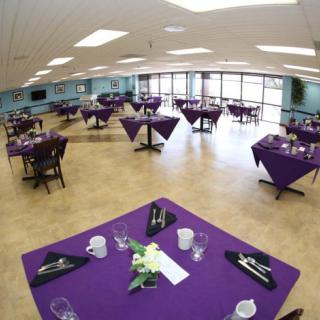 A banquet hall with tables set up with purple tablecloths, ready for an event.