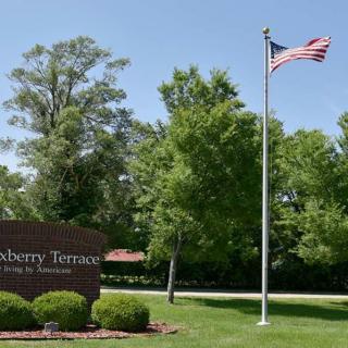 An outdoor scene with a sign, an American flag on a pole, and trees in the background.