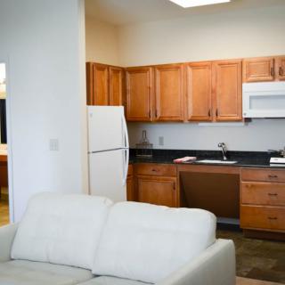 A cozy open-plan kitchen and living area featuring wooden cabinets, a refrigerator, microwave, and a comfortable white sofa.