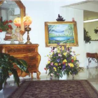 A tastefully decorated room features a wooden dresser, colorful flowers, a framed landscape painting, and an elegant mirror.