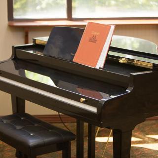 A black grand piano with sheet music open on the stand in a sunlit room.