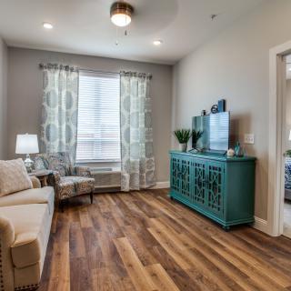 A cozy living room with modern decor, featuring a hardwood floor, a comfortable sofa and armchair, and a stylish cabinet.