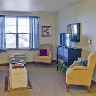 A cozy living room with comfortable chairs and a television, featuring neutral colors and natural light from the window.