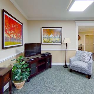 A cozy living room featuring a television, armchair, and vibrant artwork on the walls.