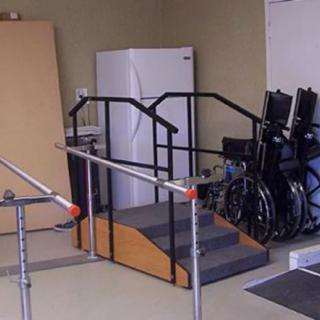 A room equipped with physical therapy tools including a ramp, parallel bars, and wheelchairs.