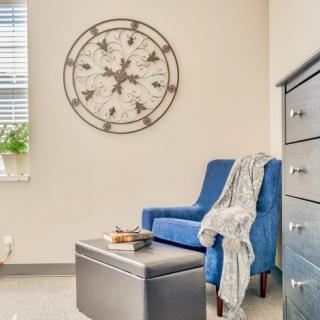 A cozy living room with a blue chair, wall clock, and a touch of greenery.