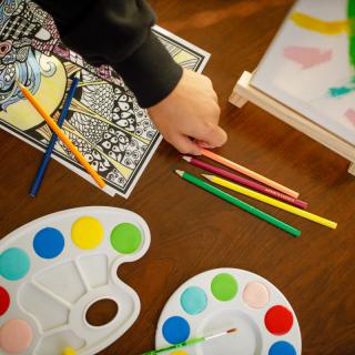 A creative setup with colored pencils, paint palettes, and coloring sheets on a table.