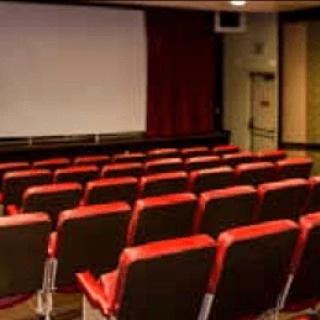 An empty theater with red seats facing a large screen.