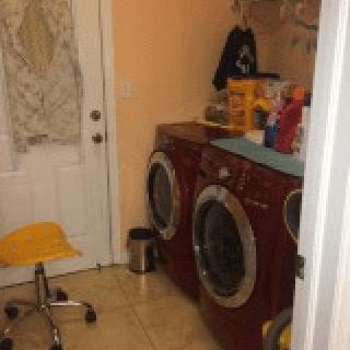 A laundry room with a washer and dryer set, accompanied by cleaning supplies and a small chair.