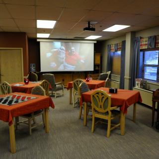 A room with several tables covered in red tablecloths, equipped with a large projector screen playing a video.