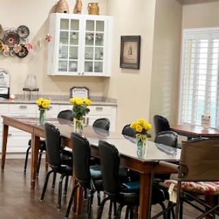 A cozy dining area featuring a long wooden table adorned with fresh flowers, surrounded by comfortable chairs and elegant cabinetry.