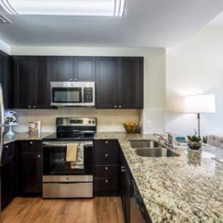 A modern kitchen with dark cabinets, granite countertops, and stainless steel appliances.