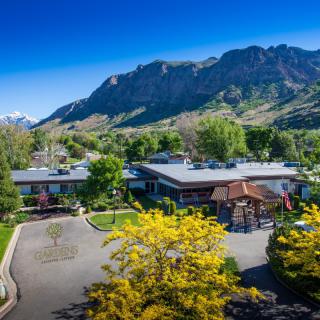 A scenic view of a building surrounded by lush greenery and majestic mountains under a clear blue sky.
