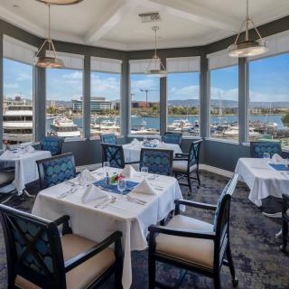 A waterfront restaurant with a scenic marina view, featuring elegantly set tables and comfortable seating.