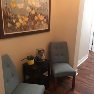 A cozy corner featuring two blue chairs and a decorative plant, complemented by a floral artwork on the wall.