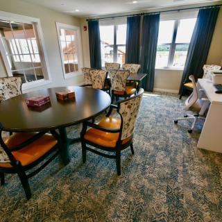 A cozy dining area featuring a round table with patterned chairs and large windows adorned with curtains.