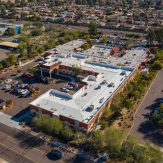 Aerial view of a large building surrounded by a parking lot and trees in an urban area.