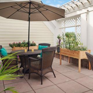 A cozy patio setup with a table, chairs, and an umbrella, surrounded by greenery and garden boxes.