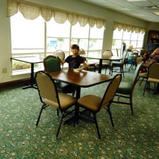 A child sitting alone at a table in a cafe with large windows and green carpet.