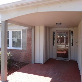 A welcoming entrance of a brick house with a covered porch and glass door.