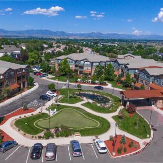 Aerial view of a residential complex with landscaped gardens and parking spaces, set against a backdrop of mountains and blue skies.