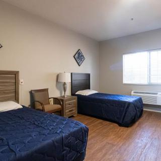A simple bedroom with two single beds, a chair, and a window allowing natural light.
