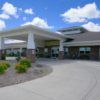 A modern building with a covered entrance and landscaped surroundings under a blue sky.