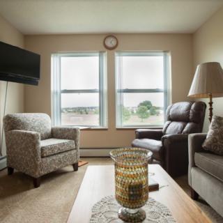 A cozy living room with armchairs, a sofa, and a coffee table in front of two large windows.