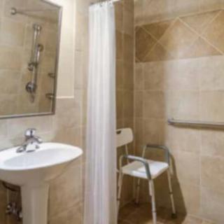An accessible bathroom with a shower, chair, and grab bar.