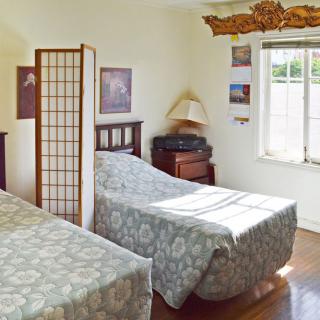 A cozy bedroom with twin beds, a screen divider, and sunlight streaming through the window.
