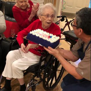 A joyful birthday celebration with an elderly woman in a wheelchair being presented a cake.