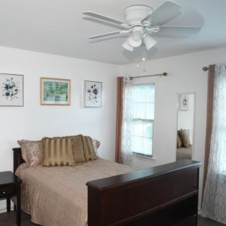 A cozy bedroom with a ceiling fan, decorated with framed wall art and light curtains.