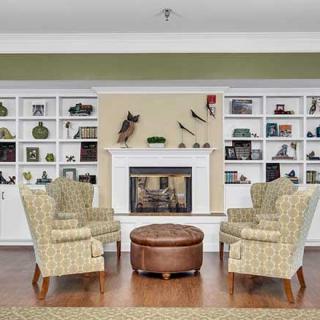 A cozy living room featuring four patterned armchairs arranged around a round coffee table, with a fireplace and decorated shelves in the background.