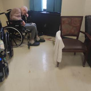 An elderly person seated in a wheelchair, lost in thought, in a quiet room.