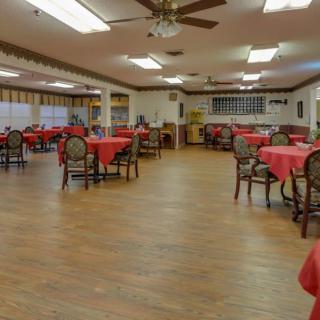 An empty dining room with red tablecloths on the tables and wooden flooring.
