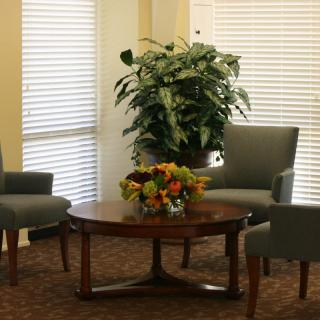 A cozy sitting area with two armchairs, a round wooden table, a large potted plant, and a floral centerpiece.