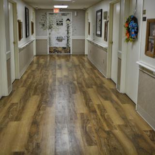 A well-lit interior hallway featuring wooden flooring and decorative wall frames.