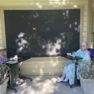 Two elderly individuals sitting outdoors enjoying coffee.