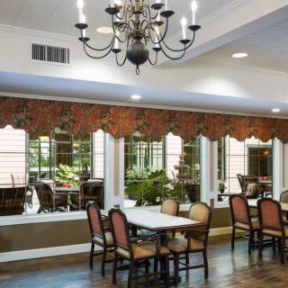 A well-decorated dining room featuring a chandelier, tables, and chairs with large windows and wall decor.