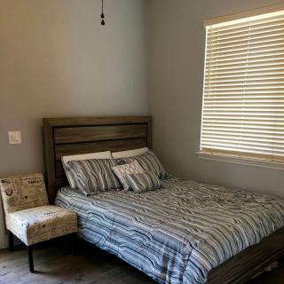 A cozy bedroom with a striped bedding set, a chair, and a window with blinds.