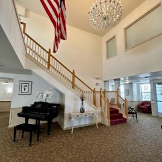 A spacious and elegantly designed lobby featuring a grand staircase, a shining chandelier, an American flag, and tasteful furnishings.