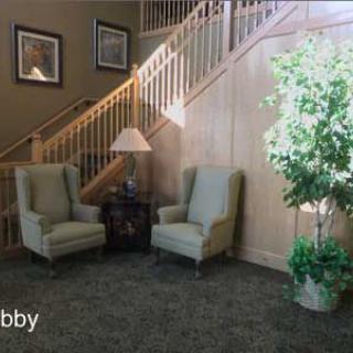 A cozy lobby area with two armchairs, a lamp, and a potted plant near a staircase.