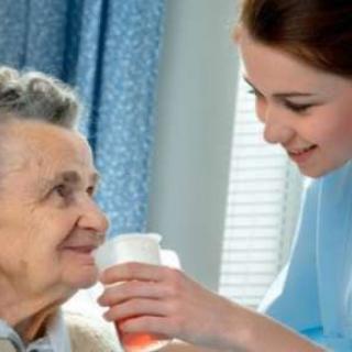 A nurse assisting an elderly woman with a drink in a healthcare setting.
