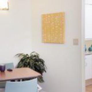 A cozy dining area with a wooden table, blue chairs, and a potted plant, complemented by abstract wall art.
